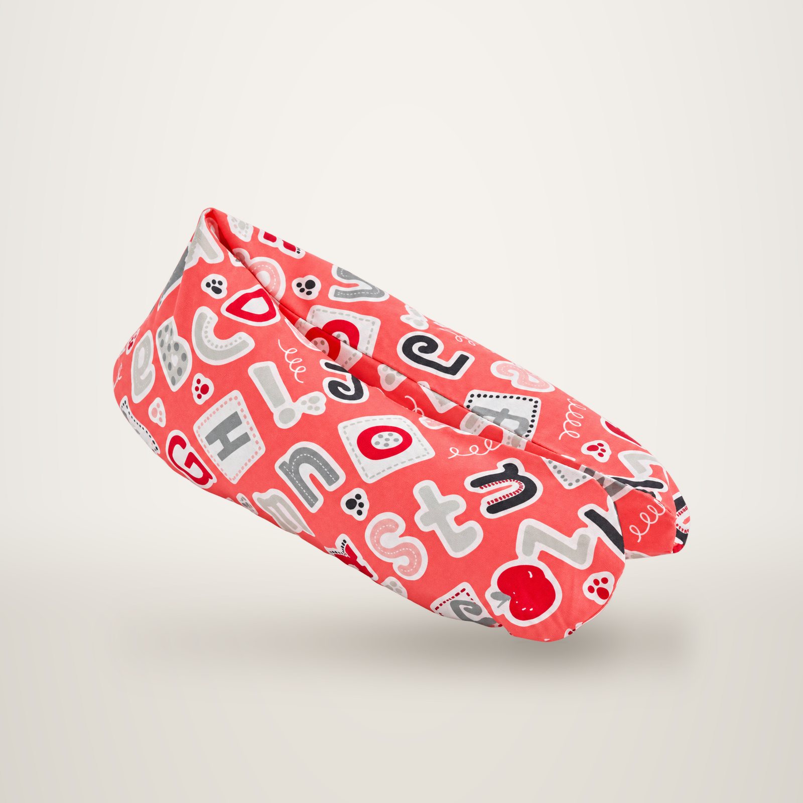 Coussin d’allaitement corail décoré de lettres de l’alphabet rouges, grises et blanches, sur fond de studio.