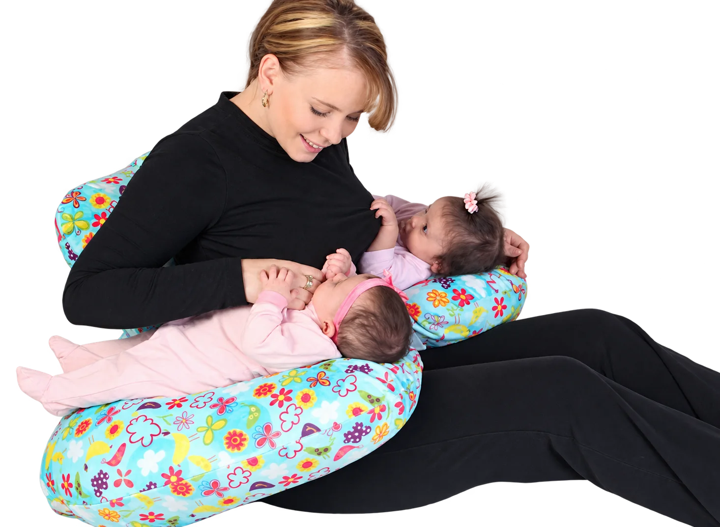 Une jeune femme en pull noir allaite deux bébés installés sur un coussin d’allaitement à motifs de fleurs et de papillons colorés.
