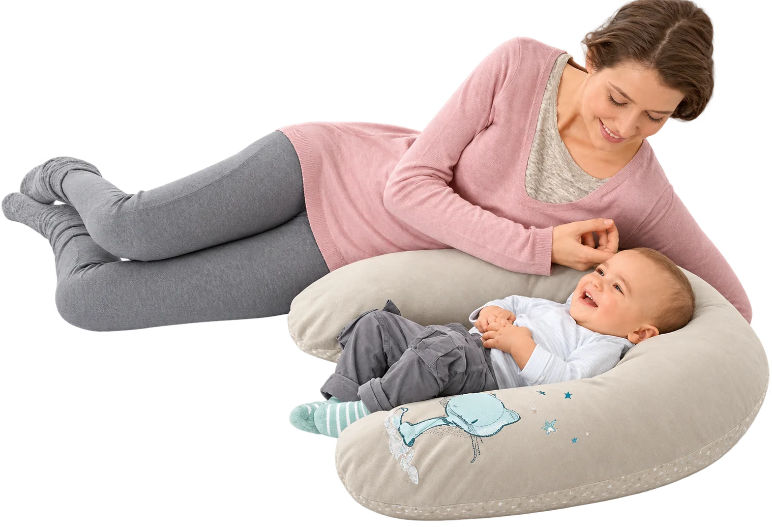 Une femme en pull rose est allongée près d’un bébé souriant installé sur un grand coussin d’allaitement beige décoré d’un motif de baleine.